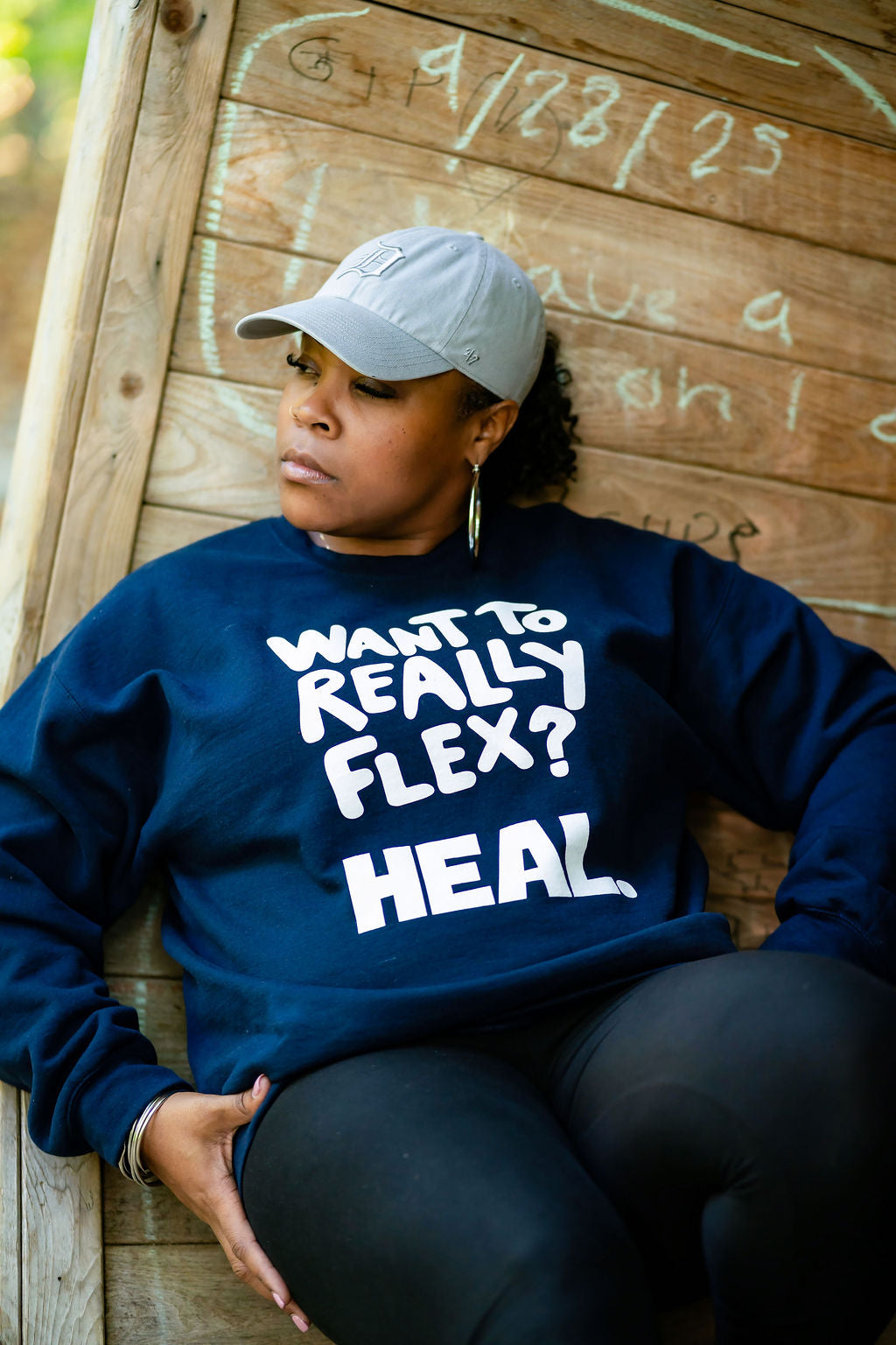 Person wearing a navy blue sweatshirt with text, sitting against a wooden wall.