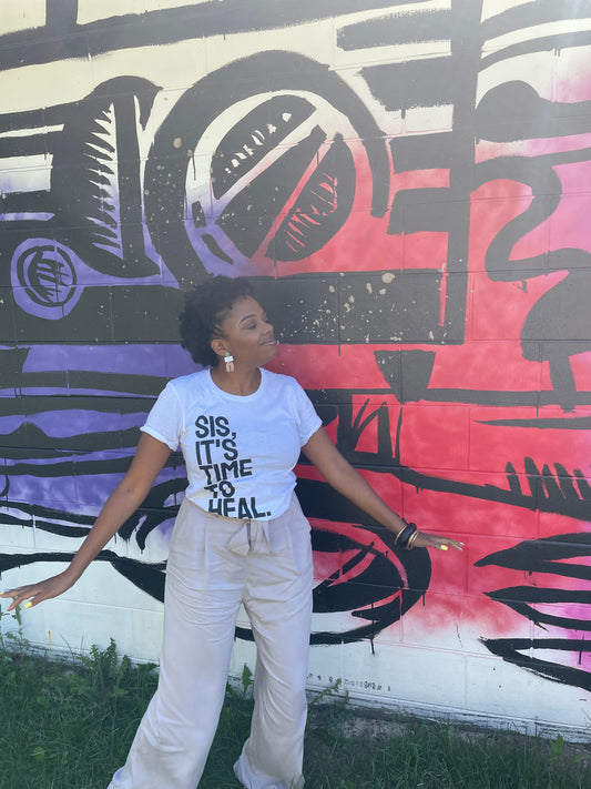 Person wearing a white t-shirt with text in front of a colorful mural.